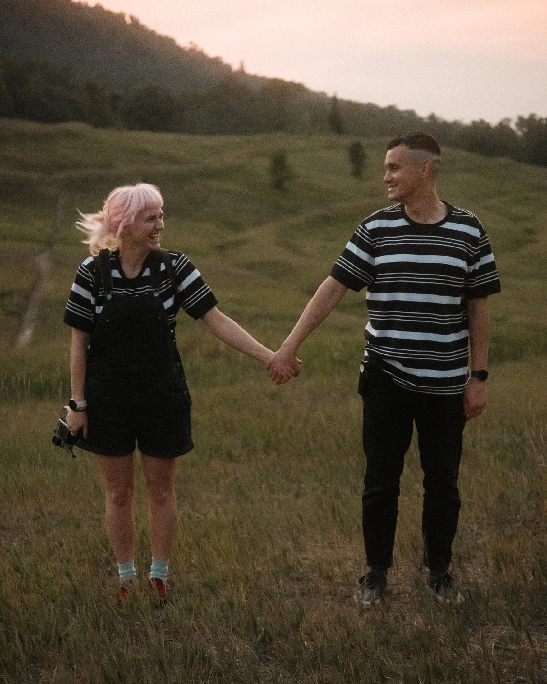 Jane and Kolya holding hands in a grassy field at sunset